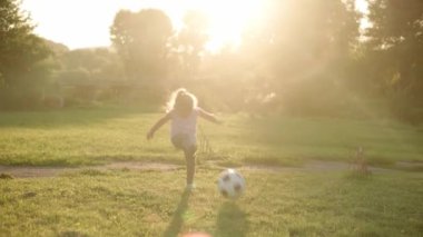 Çocukluk, oyunlar ve eğlence, spor, fiziksel kültür, parklar ve açık hava konsepti - küçük sarışın kız güneş batarken açık yeşil çimlerde siyah beyaz topla futbol oynuyor.
