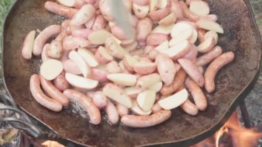 Kafeler ve restoranlar, piknik, doğu mutfağı konsepti - patatesli ve mantarlı yakın çekim sosisler dışarıda kamp ateşi üzerinde yemek pişirmek için büyük kızartma tavasında tütsülenmiş ve kızartılmış kömürlerde kızartılmış..