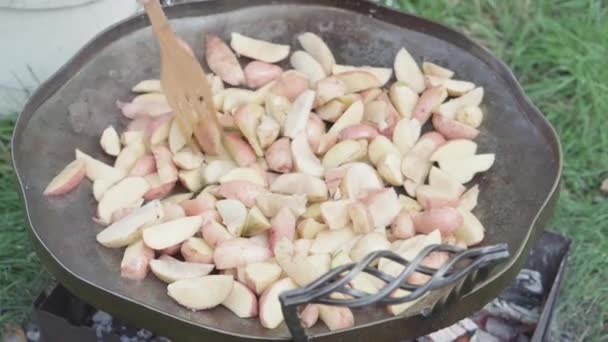 Cafés y restaurantes, cocina, picnic, concepto de cocina oriental primer plano agitar patatas con espátula de madera en una sartén enorme para cocinar alimentos sobre fogatas al aire libre: carne, verduras otros platos. — Vídeo de stock