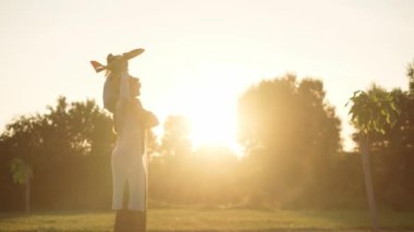 Çocukluk, oyunlar ve eğlence, spor, fiziksel kültür, açık hava konsepti - annesiyle birlikte küçük çocuklar gün batımında parkta yeşil çimlere oturup turuncu oyuncak uçak fırlatıyorlar..