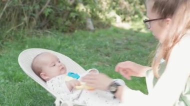 Bebeklik, çocukluk, gelişme, yaz tatili konsepti - Beş aylık uyanık bebek portresi sallanan sandalyede sallanan hamamböceğiyle oynanıyor