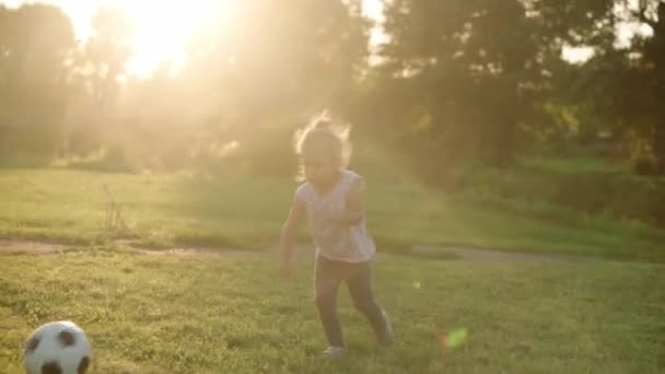 Infanzia, giochi e intrattenimento, sport, cultura fisica, parchi e concetto di aria aperta: la bambina bionda gioca a calcio con la palla in bianco e nero su un prato verde brillante nel parco estivo al tramonto. — Video Stock