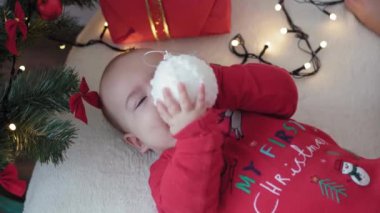 Mutlu Noeller ve mutlu yıllar, bebek, çocukluk, tatil konsepti - yakın plan 6 aylık Noel Baba şapkalı bebek ve ablasıyla kırmızı tulum Noel ağacının yanında toplarla yatıyordu.