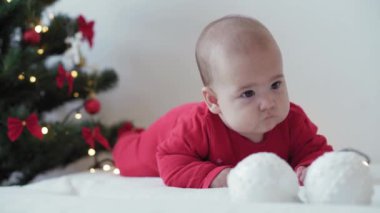 Mutlu Noeller ve mutlu yıllar, bebekler, çocukluk, tatil konsepti - yakın plan 6 aylık Noel Baba şapkalı bebek ve göbeğinde kırmızı tulum Noel ağacında süsleme toplarıyla sürünüyor