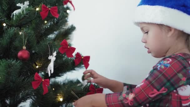 Xmas, vinter, nytt år, fest, familj koncept - glad smide liten flicka klädd i julkläder leker med dekorationer, kransar och visar känslor sitter nära dekorerade träd på kvällen — Stockvideo