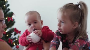 Mutlu Noeller ve mutlu yıllar, bebek, çocukluk, tatil konsepti - yakın plan 6 aylık Noel Baba şapkalı bebek ve ablası süsleme balosu yılbaşı ağacı ile sürünen kırmızı tulum