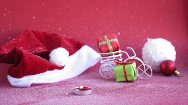 Natal, inverno, conceito de ano novo - capa de fundo de Natal vermelho com neve branca chapéu de Papai Noel com vela ardente e bicicleta de brinquedo com figurativamente presente no tronco. reorientação do primeiro plano para o segundo plano — Vídeo de Stock