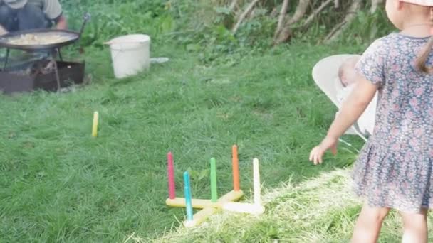 Kindertijd, kindertijd, picknick, educatieve spelletjes, ontwikkeling, zomervakantie concept - kinderen spelen Plastic Ring Toss Quoits in Garden. pasgeboren baby liggend in schommelstoel achtergrond van groen gras — Stockvideo