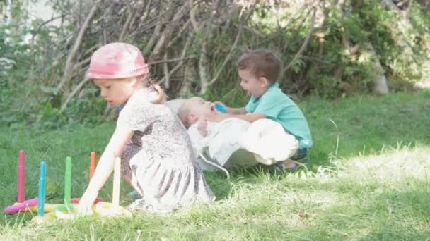 Infância, infância, piquenique, jogos educativos, desenvolvimento, conceito de férias de verão - crianças jogando plástico Ring Toss Quoits no jardim. bebê recém-nascido deitado em cadeira de balanço fundo de grama verde — Vídeo de Stock