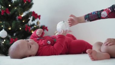 Mutlu Noeller ve mutlu yıllar, bebek, çocukluk, tatil konsepti - yakın plan 6 aylık Noel Baba şapkalı bebek ve ablası süsleme balosu yılbaşı ağacı ile sürünen kırmızı tulum