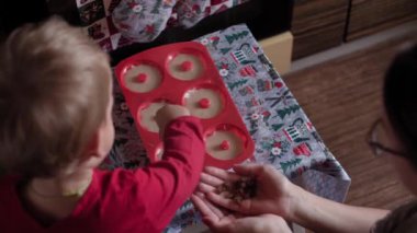 Xmas, kış, yeni yıl, kutlama, aile, fırın, hazırlık, yemek konsepti - Genç anne, Noel 'de dekore edilmiş küçük oğlu fırının yanında dururken hamur işleri hazırlıyor