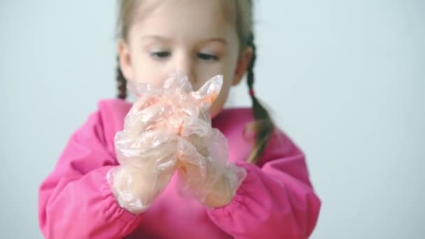 Easter, Passover, childhood, creativity, games concept - closeup of little cute blond three-year-old girl of Slovenian Caucasian appearance in pink dressing gown paints Easter eggs in plastic gloves. — Stock Video