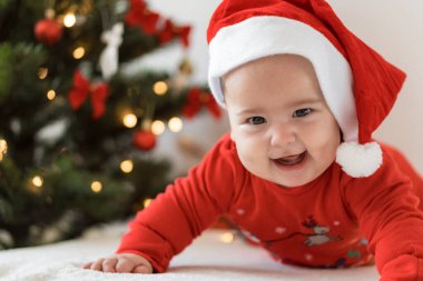 Mutlu noeller ve mutlu yıllar, bebekler, çocukluk, tatil konsepti - yakın plan çıplak bebek Noel Baba şapkalı 6 aylık bebek Noel Baba 'nın karnında Noel ağacı süslemeleri ile sürünüyor.