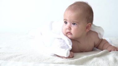 Çocukluk, günlük rutin, hijyen bebek konseptleri - banyo yaptıktan sonra beyaz arka planda mutlu çocuk havlusu. Bebek duştan sonra karın üstü yatar. Bebek yatmadan önce uyanma zamanı.
