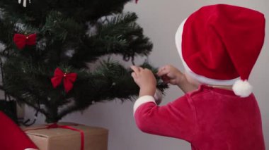 Xmas, kış, yeni yıl, kutlama, aile konsepti - iki kardeş yumuşak battaniyeye sarılmış bebek ve Noel kıyafetleri giymiş erkek kardeş ve şömine süslenmiş Noel ağacı başında şapka oyunu