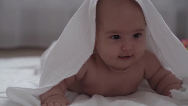 Médecine, soins de santé, famille, innocence, pédiatrie, bonheur, concepts pour bébés Gros plan sourire nu 4 mois bébé jouer sur le ventre couché dans la crèche sur le sol avec une serviette sur la tête après le bain — Video