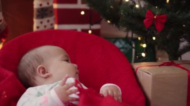 Xmas, kış, yeni yıl, kutlama, aile konsepti Noel kıyafetleri içinde sallanan sandalyeye oturmuş şöminenin ve Noel ağacının yanında sıcak kırmızı battaniyeye sarılmış güzel bir bebek..