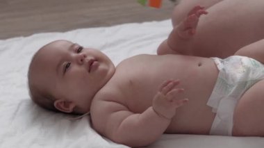 Tıp, sağlık, aile, masumiyet, pediatri, mutluluk, bebek konseptleri - anne motivasyon öğretir, bebeği tekrar karnına döndürür, masaj ve egzersiz, beyaz yatakta renkli oyuncaklara ulaşır