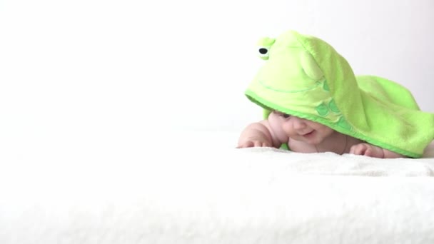 Dětství, každodenní rutina, hygienické kojenecké koncepty - Detailní záběr Šťastné dítě barevný ručník zelené žáby na bílém pozadí po koupeli. novorozenec po sprše na břiše v posteli. čas probuzení dítěte — Stock video