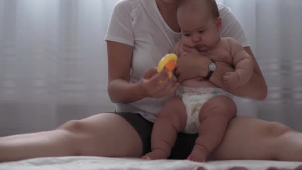 Médecine, soins de santé, famille, innocence, pédiatrie, bonheur, concepts de bébé - Jeune mère heureuse tenant nue bébé de 4 mois et jouant avec un jouet coloré cafard assis dans la crèche sur le sol — Video