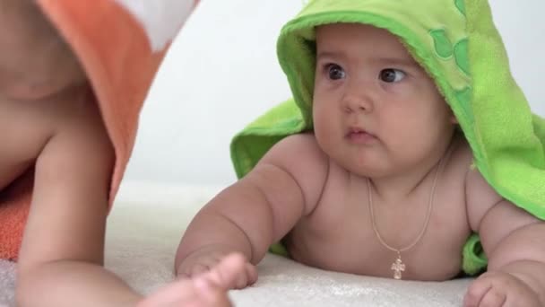 Enfance, routine quotidienne, concepts d'hygiène - Gros plan Deux enfants heureux en peignoir sur fond blanc après avoir pris un bain. fille et nouveau-né après la douche sur le ventre sur le lit. Jumeaux irlandais avec coloré — Video