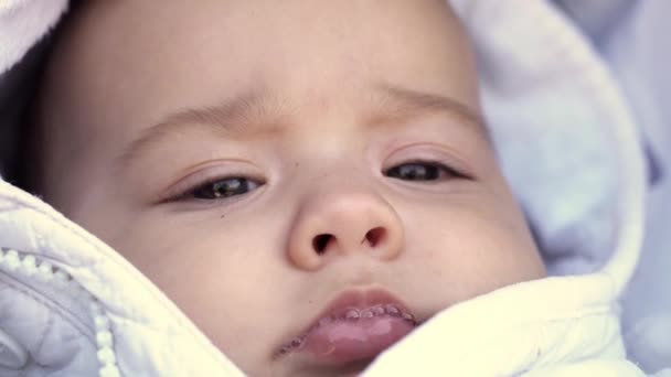 Niemowlę, dzieciństwo, koncepcja emocji - zbliżenie uroczej uśmiechniętej twarzy brązowookiego pulchnego noworodka bezzębnego dziecka w wieku 6 miesięcy patrzącego na kamerę leżącą w białej kurtce w wózku z śliniącymi się ustami — Wideo stockowe
