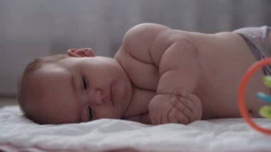 Tıp, sağlık, aile, masumiyet, pediatri, mutluluk, bebek konseptleri - Anne motivasyon öğretiyor. Bebek yuvarlanması, sırt üstü dönme, masaj ve egzersiz, beyaz yatakta renkli oyuncaklara ulaşma