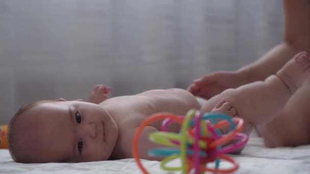 Medizin, Gesundheitswesen, Familie, Unschuld, Pädiatrie, Glück, Säuglingskonzepte - Mama lehrt Motiviert Babys vom Rücken in den Bauch, massiert und trainiert, greift zu farbigem Spielzeug auf weißem Bett zu Hause — Stockvideo