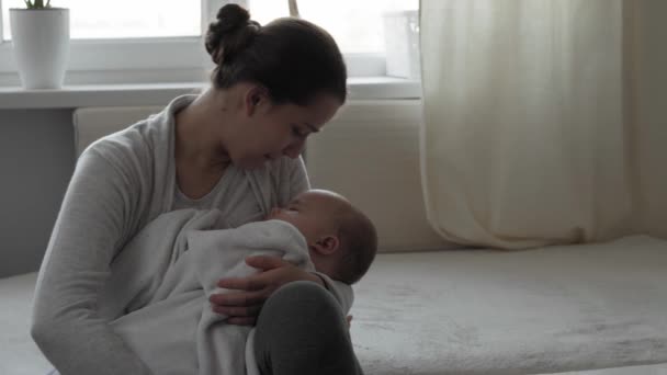 Médecine, soins de santé, famille, innocence, pédiatrie, bonheur, concepts de bébé - Jeune mère heureuse tenant le sommeil 7 mois fille bébé fille rock dans les bras et chanter berceuse assis dans la crèche sur le lit — Video