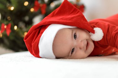 Mutlu noeller ve mutlu yıllar, bebekler, çocukluk, tatil konsepti - yakın plan çıplak bebek Noel Baba şapkalı 6 aylık bebek Noel Baba 'nın karnında Noel ağacı süslemeleri ile sürünüyor.