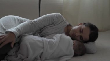 Tıp, sağlık, aile, masumiyet, pediatri, mutluluk, bebek konseptleri - Genç mutlu anne uykulu bir şekilde yatıyordu. Sıcak battaniyeyle örtülmüş bebek kız çocuğu ve ninni söylüyordu.