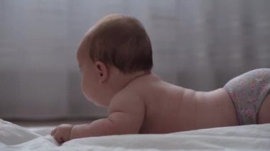 Tıp, sağlık, aile, masumiyet, pediatri, mutluluk, bebek konseptleri - anne motivasyon öğretir, bebeği tekrar karnına döndürür, masaj ve egzersiz, beyaz yatakta renkli oyuncaklara ulaşır
