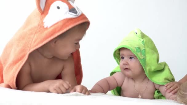 Παιδική ηλικία, καθημερινή ρουτίνα, έννοιες υγιεινής - Τρία ευτυχισμένα παιδιά σε μπουρνούζια σε λευκό φόντο μετά το μπάνιο. κορίτσι και νεογέννητο μετά το ντους στο στομάχι στο κρεβάτι. Ιρλανδοί δίδυμοι με πετσέτα πριν κοιμηθούν — Αρχείο Βίντεο