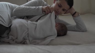 Tıp, sağlık, aile, masumiyet, pediatri, mutluluk, bebek konseptleri - Genç mutlu anne uykulu bir şekilde yatıyordu. Sıcak battaniyeyle örtülmüş bebek kız çocuğu ve ninni söylüyordu.