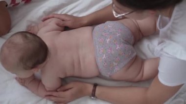Tıp, sağlık, aile, masumiyet, pediatri, mutluluk, bebek konseptleri - anne bebeklere sırt çevirmeyi, masaj ve egzersiz yapmayı, evde beyaz yatakta cilt veya göğüs masajı yapmayı öğretiyor.