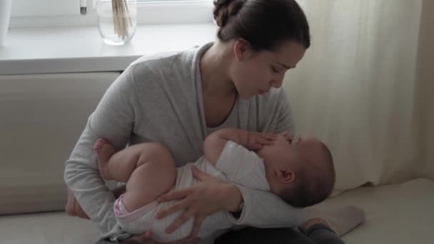 Medycyna, opieka zdrowotna, rodzina, niewinność, pediatria, szczęście, koncepcje niemowląt - młoda szczęśliwa matka uczy się siadać 7-miesięczne pocałunki dziecka, pieszczoty siedzące w jasnym słońcu żłobka na miękkim łóżku — Wideo stockowe