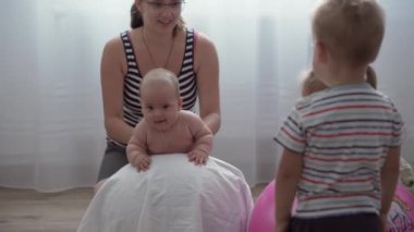 Çocukluk, annelik, oyunlar, terbiye, gelişim konsepti - genç anne egzersiz yapıyor, yeni doğmuş bebekle spor yapıyor. Küçük kız ve erkek çocuk oyun odasında gülüp oynuyorlar. Kreşteki çocuklar