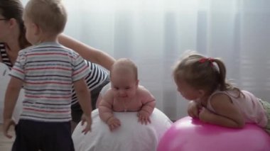 Çocukluk, annelik, oyunlar, terbiye, gelişim konsepti - genç anne egzersiz yapıyor, yeni doğmuş bebekle spor yapıyor. Küçük kız ve erkek çocuk oyun odasında gülüp oynuyorlar. Kreşteki çocuklar