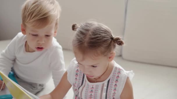 Family, innocence, infant concepts - Two smiling children read large interesting book of fairy tales on bed. Siblings little boy and girl brother and sister have fun, happy kids on quarantine at home — Stock Video