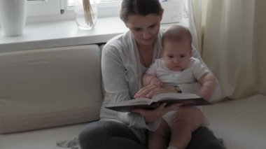 Tıp, sağlık, aile, masumiyet, pediatri, mutluluk, bebek konseptleri - Genç mutlu anne kitap okur ve tombul bebekle oynar.