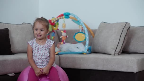 Dětství, hry, výchova a rozvoj koncept -holčička skáče na růžové knot na pozadí novorozená sestra leží na podložce ve vývojové dětské herně. Sourozenci se baví doma na karanténě.