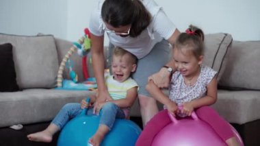 Çocukluk, oyunlar, yetiştirme ve geliştirme konsepti. Küçük çocukların genel planı. Erkek kardeş ve kız kardeş, annesi çocuk oyun odasında Fitball 'a atlıyor. Kardeşlerin karantinadaki evleri eğlencelidir.