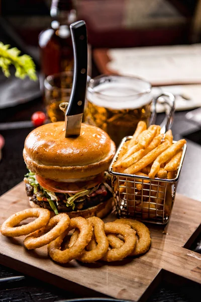 Beef burger with fries in rustic style on fabric with glass bear. rings of onion