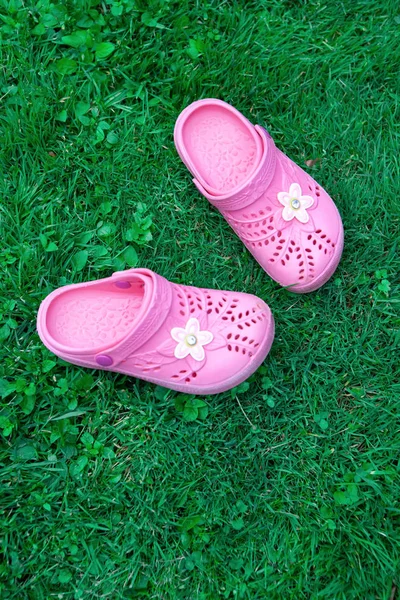 Pink kid\'s slippers on green lawn. Top view, in the middle of frame. Vertical. Concept of vacation with children, unity with nature. Mock up for children\'s store product, mother\'s blog