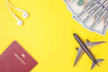 Yüz dolar faturaları, uçak, kulaklık, parlak sarı kağıt arka plan yabancı pasaportla. Uzay kopyalayın. Seyahat ve bütçe seyahat kavramı, düz yatıyordu. El bagajı, minimalizm, çerçeve nesneler.