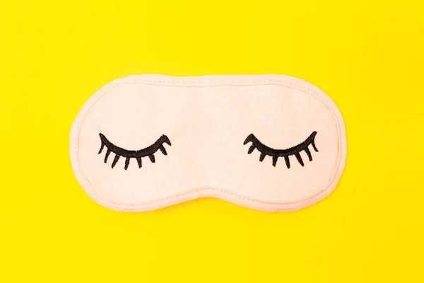 Máscara para dormir rosa pastel con los ojos cerrados bordados en ella con pestañas sobre fondo de neón amarillo brillante. Accesorio de moda para dormir. Concepto de sueños vívidos, accesorios para niñas y mujeres jóvenes . — Foto de Stock