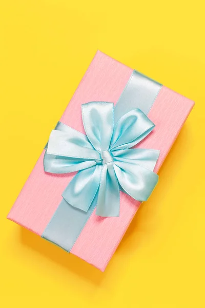 Sarı arka planda üst yay ile mavi şerit ile bağlı pembe hediye kutusu. Dikey. Minimal düz yatmak. Üst görünüm. Doğum günü, yeni yıl, anneler günü, kadın günü kutlama kavramı