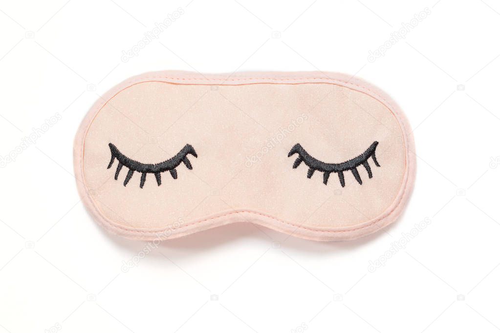 Pastel pink sleep mask with closed eyes embroidered on it with eyelashes on white background. Top view, flat lay. Concept of vivid dreams. Accessories for girls and young women.