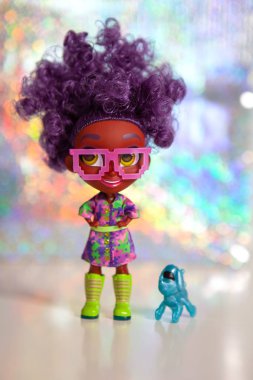 Moskova, Rusya - 18 Nisan 2019: Doll surprise Hairdorables. Seri 1. Kalın kıvırcık saçlı gözlüklü koyu tenli bebek. Evcil köpek robotuyla. Renkli hologram bokeh arka plan.