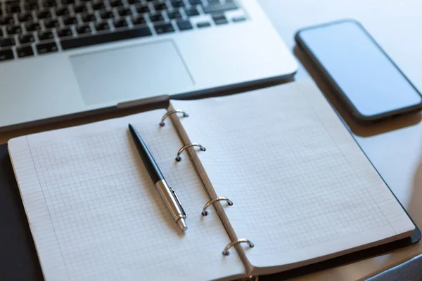 Werkruimte, bovenaanzicht. Laptop, mobiele telefoon en open notebook met pen op beige desktop. Notitieblokjes op zilveren beugels, automatische balpen in zilverkleurige kleur. Bedrijfsachtergrond. — Stockfoto